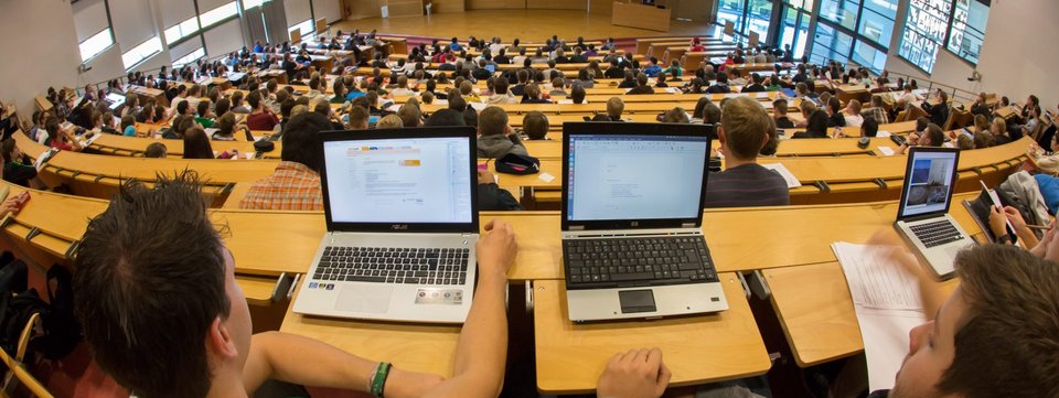 Studentinnen und Studenten hören eine Vorlesung im Hörsaal, zwei Laptops sind zu sehen