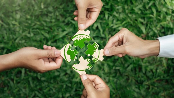 Vier Hände die je ein Puzzleteil mit grüner Erde in der Mitte zusammenführen