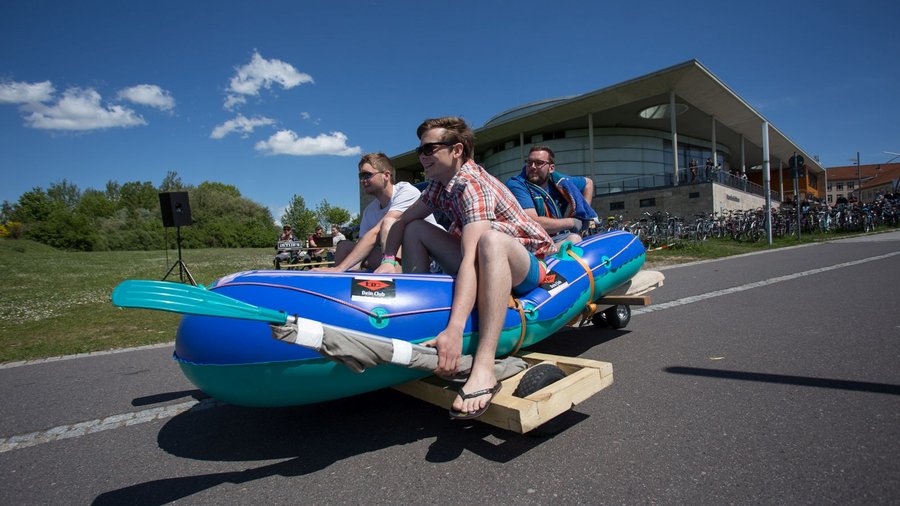 Studierende "fahren" im Boot eine Straße hinunter