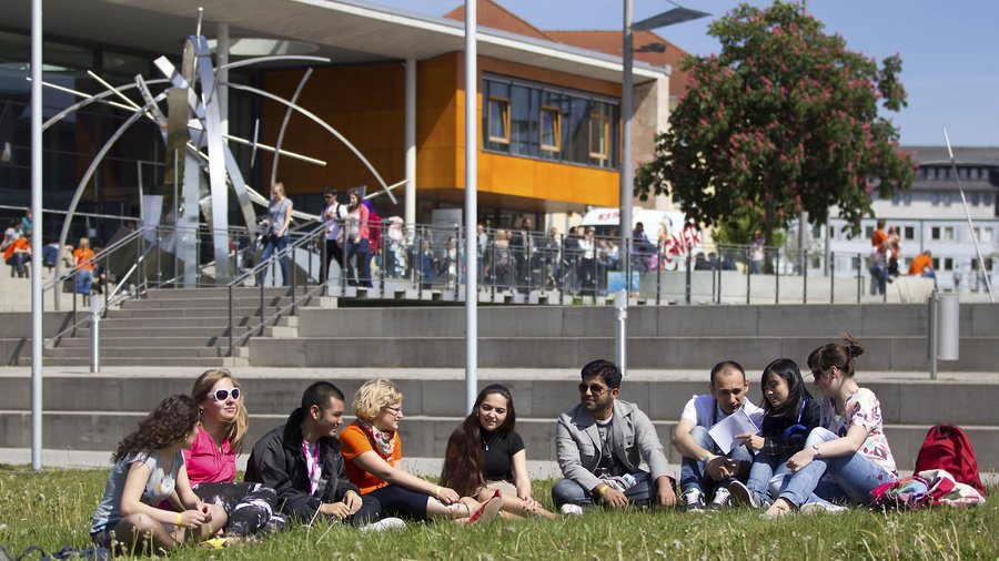 Mehrere Studierende sitzen vor dem Audimax im Gras