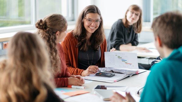 Student*innen sitzen am Tisch mit Lernmaterialien