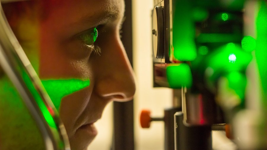 Auge einer Frau, die in Gerät des opthalmologischen Labors schaut, wird grün erleuchtet 