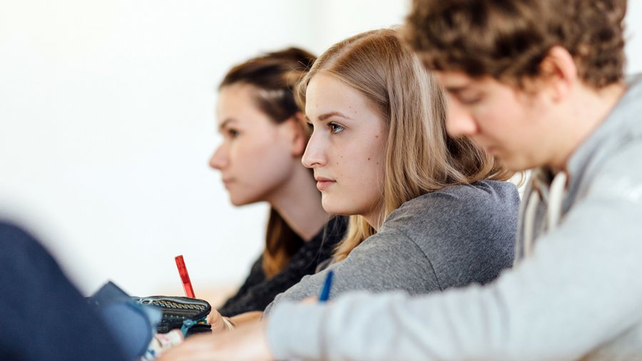 Drei Studierende machen Notizen in Seminar.
