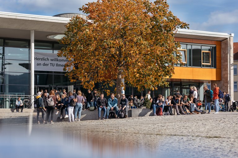 Unigebäude mit Studierenden und großem Baum im Vordergrund