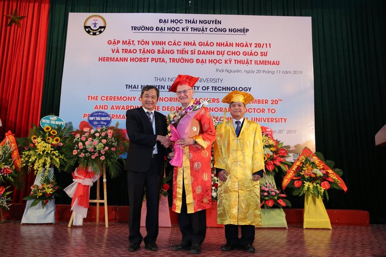 Prof. Horst Puta, der Präsident und der Vizepräsident der vietnamesischen Partneruni stehen zur Verleihung der Ehrendoktorwürde an Prof. Puta auf der Bühne.