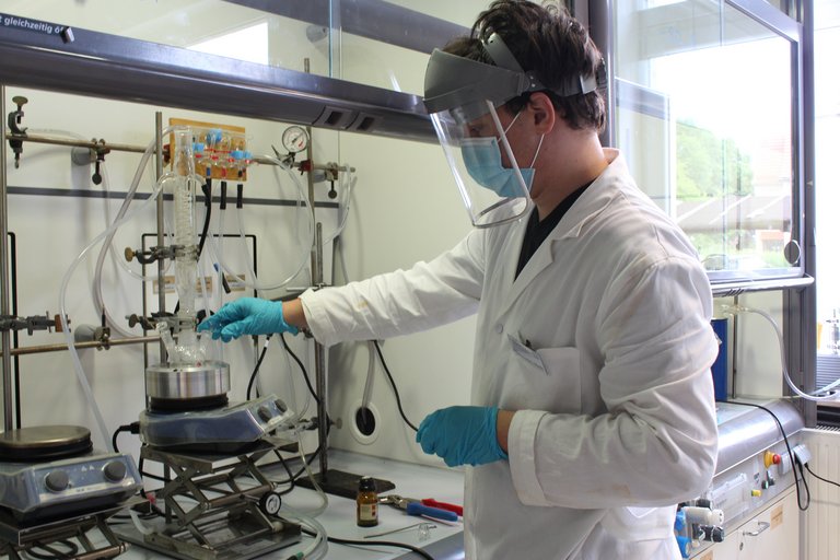 Student with smock and face visor at the fume hood of the chemistry lab