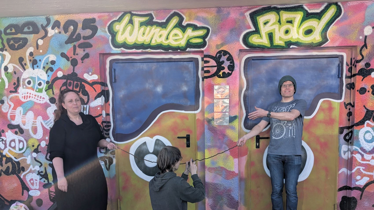 Drei Personen beim Durschneiden eines Bands vor Fahrradwerkstatt