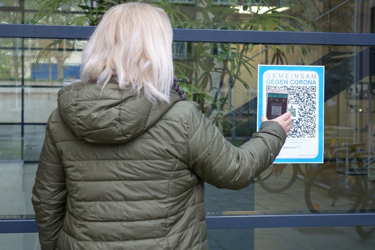 Employee stands by a sign with a QR code and scans it with her cell phone.